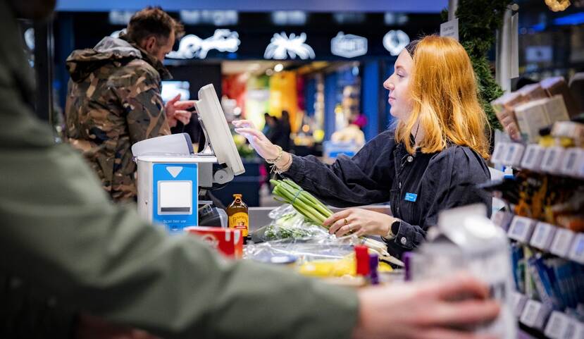 Een loopband van een kassa met boodschappen, een kassamedewerker slaat de boodschappen aan