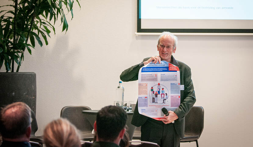 Voorzitter van het College voor de Rechten van de Mens Jos Silvis presenteert de poster 'Samen tegen armoede' tijdens een bijeenkomst van het Platform Gemeenten en Mensenrechten.