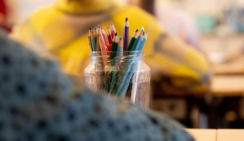 Pot met gekleurde potloden in een klas tussen twee kinderen, op de rug gezien.
