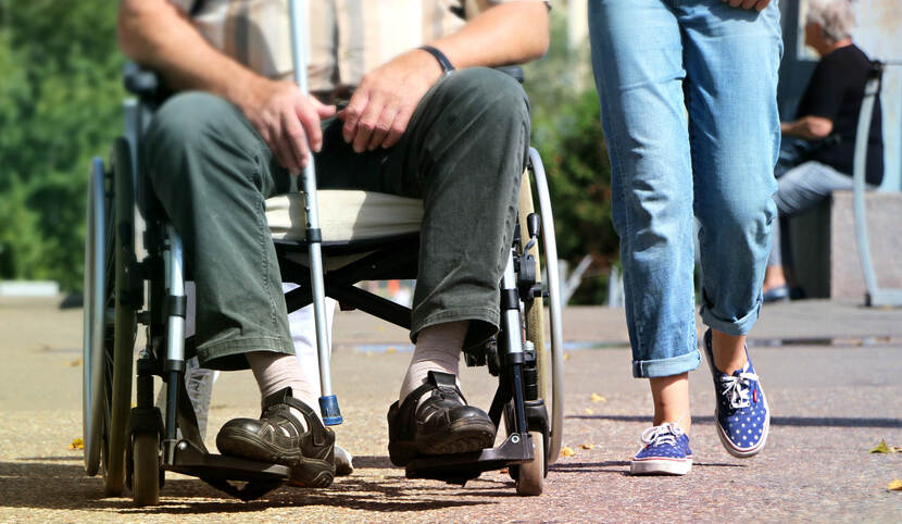 Man in rolstoel buiten met naast zich wandelende vrouw