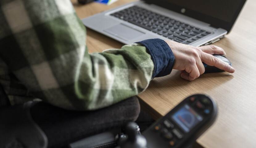 Man in rolstoel werkt op zijn laptop