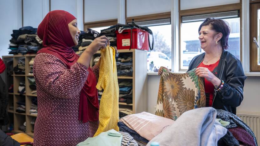 Twee vrijwilligers vouwen kleding op bij de kledingbank