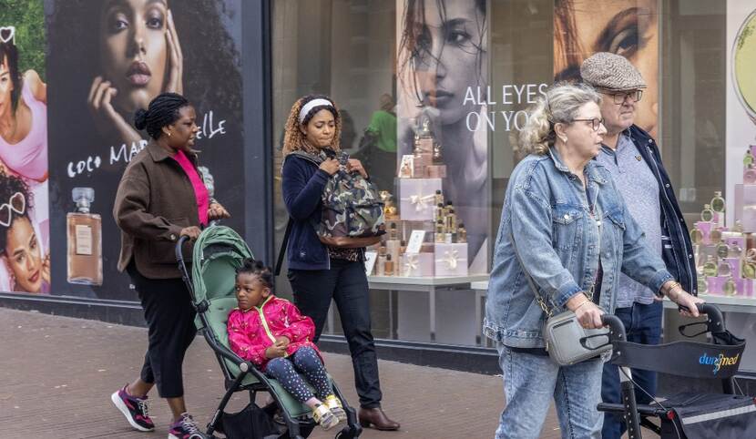 Passanten lopen langs etalage en gote reklameborden van Parfumerie Douglas.