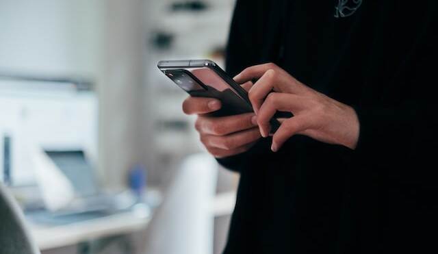 Een vrouw houdt een smartphone vast, je ziet alleen haar handen.