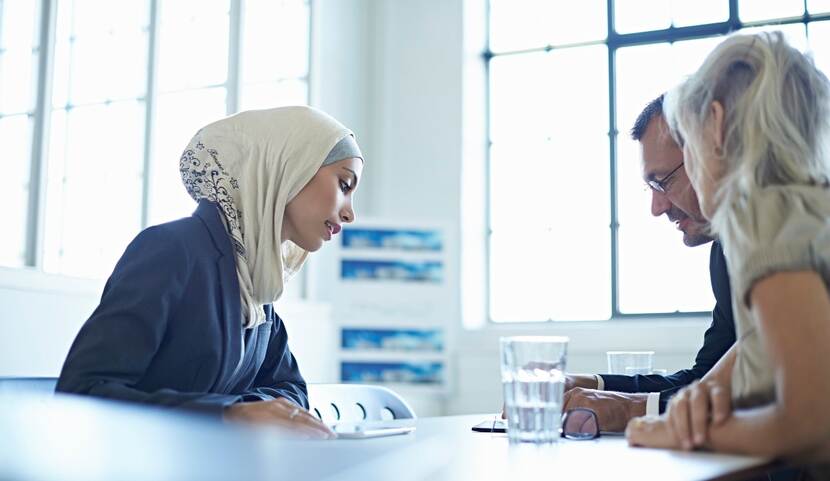 Drie collega's overleggen aan een bureau, een van hen draagt een hoofddoek